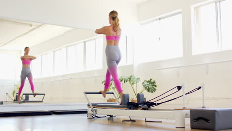 Caucasian-woman-in-pink-bra,-purple-leggings-exercises-on-Pilates-reformer