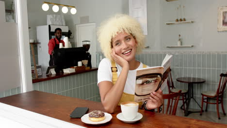 Una-Joven-Birracial-Con-Cabello-Rubio-Rizado-Sonríe-Mientras-Lee-Un-Libro-En-Un-Café