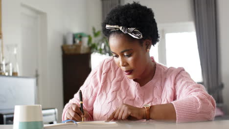 African-American-woman-writes-in-a-notebook-at-a-desk-at-home
