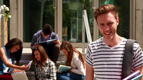 Smiling-student-posing-and-friends-studying-behind-him