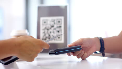 A-person-is-handing-over-credit-card-to-another,-with-a-QR-code-in-background