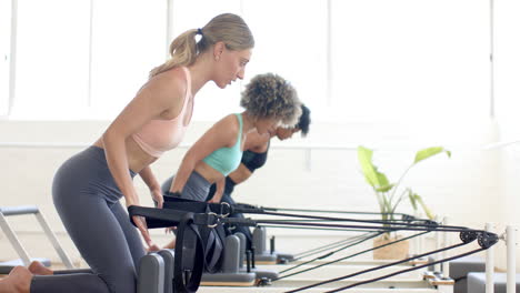 Two-women-practicing-on-pilates-reformer-machines-in-bright-studio