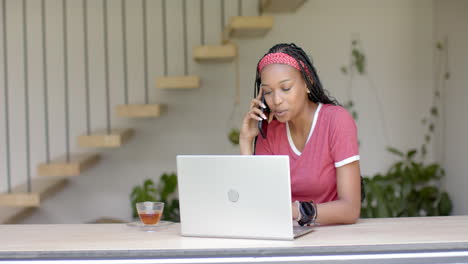 Mujer-Joven-Afroamericana-Hablando-Por-Teléfono,-Trabajando-En-Una-Computadora-Portátil-En-Casa