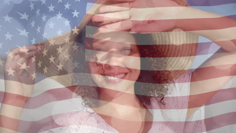 Animation-Von-Lichtpunkten-Und-Amerikanischer-Flagge-über-Einer-Gemischtrassigen-Frau-Mit-Sonnenhut,-Die-Am-Sonnigen-Strand-Lächelt