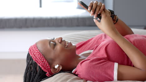Afroamerikanische-Junge-Frau-Liegt,-Hält-Smartphone,-Lacht