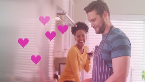 Animation-of-hearts-over-diverse-couple-cooking-together-and-drinking-wine-in-kitchen-at-home