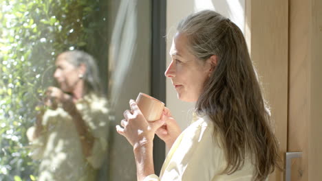 A-mature-Caucasian-woman-holding-cup,-looking-out-window