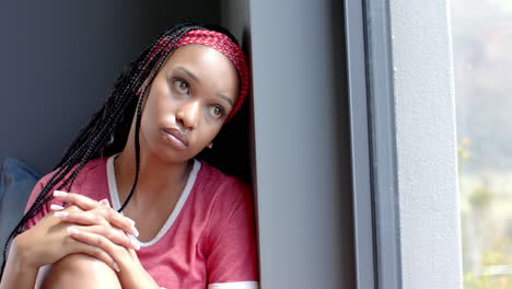 Eine-Junge-Afroamerikanische-Frau,-Die-Am-Fenster-Sitzt-Und-Nach-Draußen-Schaut