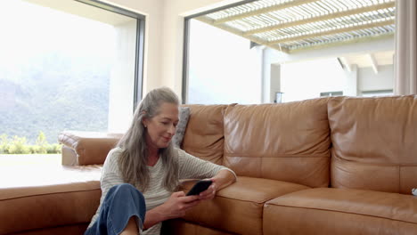 Caucasian-mature-woman-sitting-on-sofa,-looking-at-smartphone