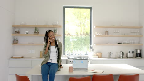 African-American-young-woman-talking-on-phone,-sitting-in-kitchen