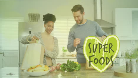 Animation-of-super-foods-text-over-diverse-couple-preparing-healthy-meal-in-kitchen