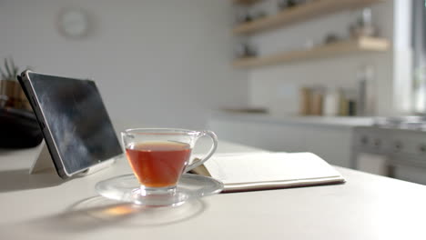 A-tablet-and-cup-of-tea-rest-on-a-kitchen-counter-beside-open-notebook