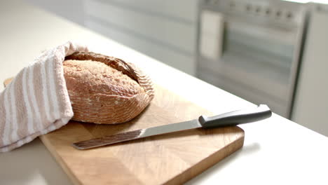 Freshly-baked-bread-resting-on-wooden-cutting-board-with-a-knife-beside-it
