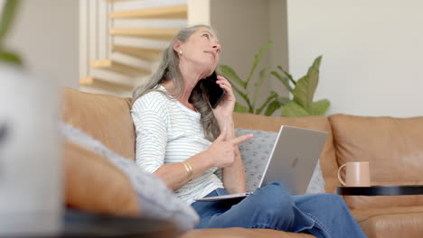 Caucasian-woman-with-gray-hair-talking-on-phone,-using-laptop