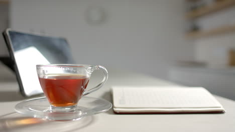 A-cup-of-tea-sits-on-saucer-next-to-open-notebook-on-a-desk