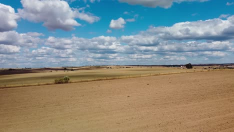 Sonnige-Ländliche-Landschaft-Mit-Weiten-Offenen-Feldern-Und-Einem-Strahlend-Blauen-Himmel-Voller-Flauschiger-Wolken