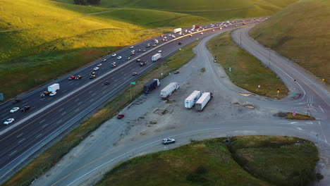 Aerial-view-toward-trucks-at-a-truckstop-at-a-highway,-sunset-in-California,-USA