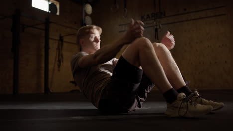 Caucasian-man-does-sit-up-workout-routine-in-gym,-cinematic-light