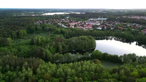 Panorama,-drone-view-of-a-landscape-featuring-a-forest,-lake,-and-city-buildings-in-the-distance