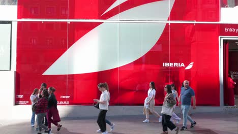 Wide-view-shot-of-pedestrians-walking-past-the-Spanish-airline-Iberia's-pop-up-store-on-the-retail-and-entertainment-street-of-Gran-Via-in-Madrid,-Spain