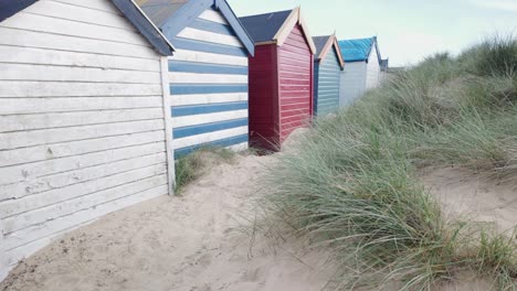 Rear-of-Colourful-beach-huts-along-the-sand-dunes,-Southwold