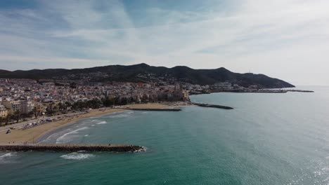 Küste-Von-Sitges-Und-Stadtbild-Mit-Bergen-Im-Hintergrund,-Luftaufnahme