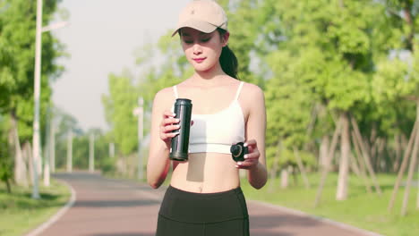 Portrait-beautiful-girl-athlete-taking-a-break-during-the-race-to-hydrate-exercise,-sportswoman-in-sportswear-drinking-water-from-bottle-while-jogging-exercise-at-public-park-in-the-morning
