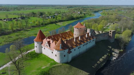 Aerial-establishing-view-of-Bauska-Medieval-Castle-and-ruins,-Musa-and-Memele-rivers-next-to-the-castle,-sunny-spring-day,-wide-orbiting-drone-shot
