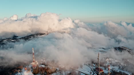 Snowy-mountain-with-communication-towers-above-clouds-at-sunrise