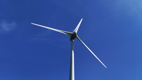 Turbina-Eólica-Girando-Contra-Un-Cielo-Azul-Claro,-Capturada-Desde-Un-ángulo-Bajo