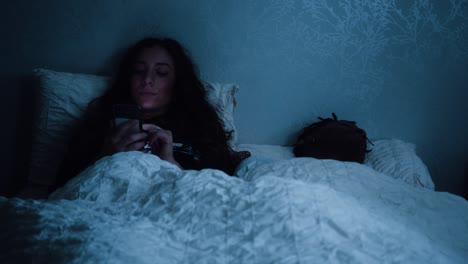 Woman-scrolls-through-her-phone-whilst-sat-in-bed-at-night