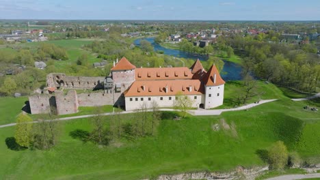 Aerial-establishing-view-of-Bauska-Medieval-Castle-and-ruins,-Musa-and-Memele-rivers-next-to-the-castle,-sunny-spring-day,-distant-wide-orbiting-drone-shot