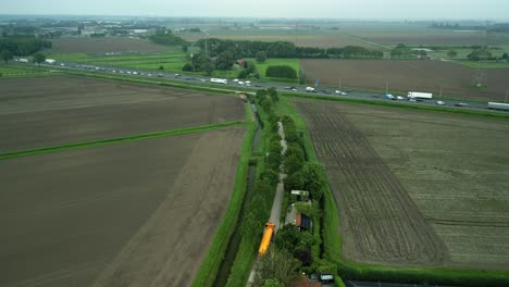 Landscape-with-national-highway,-high-voltage-pylons,-farmers'-fields-and-an-orange-tanker-truck-on-a-country-road