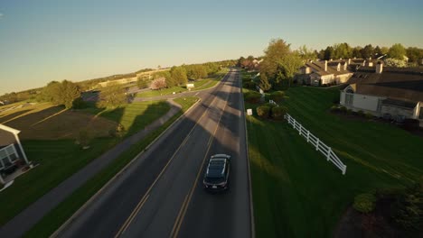 Fpv-following-black-car-on-road-of-American-suburbia-during-sunset-time