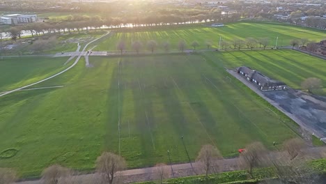 A-top-view-shot-over-the-ornamental-pond-of-Nottingham-War-Memorial-Gardens-and-Meadows-Recreation-Ground:-vivid-green-fields-are-illuminated-by-sunset-rays