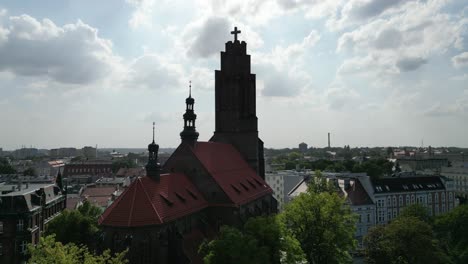 Medieval-church-during-a-beautiful-summer-day-surrounded-by-lush-greenery,-grass,-buildings-and-trees-under-a-blue-sky