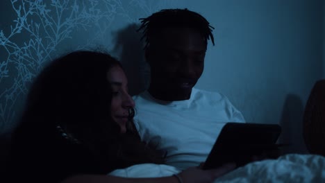 Young-couple-sitting-up-in-bed-at-night-watching-a-tablet-device