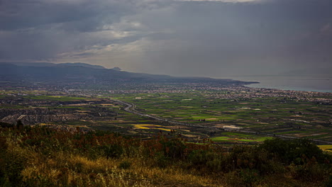 Time-lapse-establishing-rural-countryside-village-landscape,-mountain-background,-clouds-in-motion,-cars-driving-by