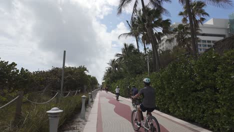 Miami-Beach-boardwalk-with-cyclist-under-palm-trees-and-partly-cloudy-sky