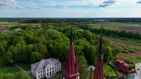 A-church-tower-in-lush-green-lithuanian-countryside-under-a-blue-sky,-aerial-view