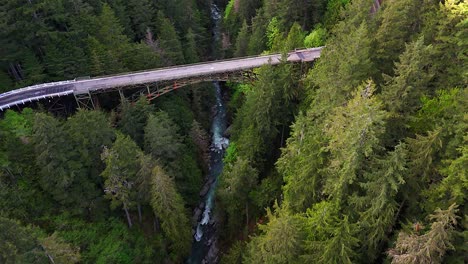 Scenic-Aerial-shot-flying-over-flowing-river-and-evergreen-forest-with-a-steel-bridge-in-Carbonado,-Washington-state