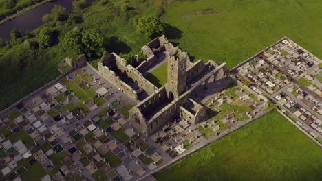 Claregalway-Friary-ruins-with-cloud-shadow-rushing-over-tombstones-and-cemetery,-view-from-above
