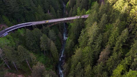 Scenic-aerial-descending-shot-over-flowing-river-in-evergreen-forest-show-casing-steel-bridge-in-Carbonado,-Washington-State