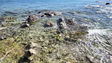 Crystal-clear-water-and-rocky-sea-bed-at-the-coastline-of-Pafos,-Cyprus,-with-gentle-waves-lapping-against-the-shore