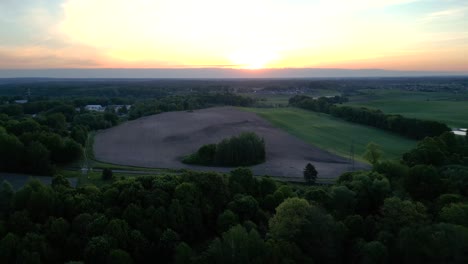 Panorama-at-sunset,-view-of-a-landscape-featuring-a-forest,-fields,-and-the-setting-sun