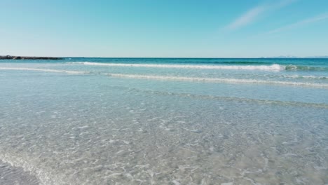 Walking-on-the-sandy-beach-towards-the-waves-and-turquoise-sea-waters-on-a-sunny-spring-day