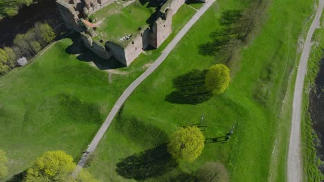 Aerial-establishing-view-of-Bauska-Medieval-Castle-and-ruins,-Musa-and-Memele-rivers-next-to-the-castle,-sunny-spring-day,-drone-shot-moving-backward,-camera-tilt-up