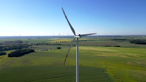 Close-up-of-a-wind-turbine-with-others-in-the-background,-rapeseed-field,-and-blue-sky,-renewable-energy-sources