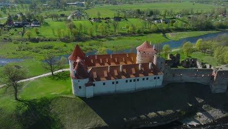 Aerial-establishing-view-of-Bauska-Medieval-Castle-and-ruins,-Musa-and-Memele-rivers-next-to-the-castle,-sunny-spring-day,-wide-drone-shot-moving-forward,-camera-tilt-down