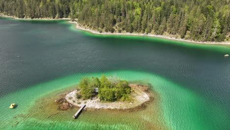 Aerial-view-of-a-small,-lush-green-island-with-a-wooden-pier,-surrounded-by-the-clear,-turquoise-waters-of-Seerenbachfälle-Lake,-located-in-Amden-Betlis,-Walensee,-Switzerland